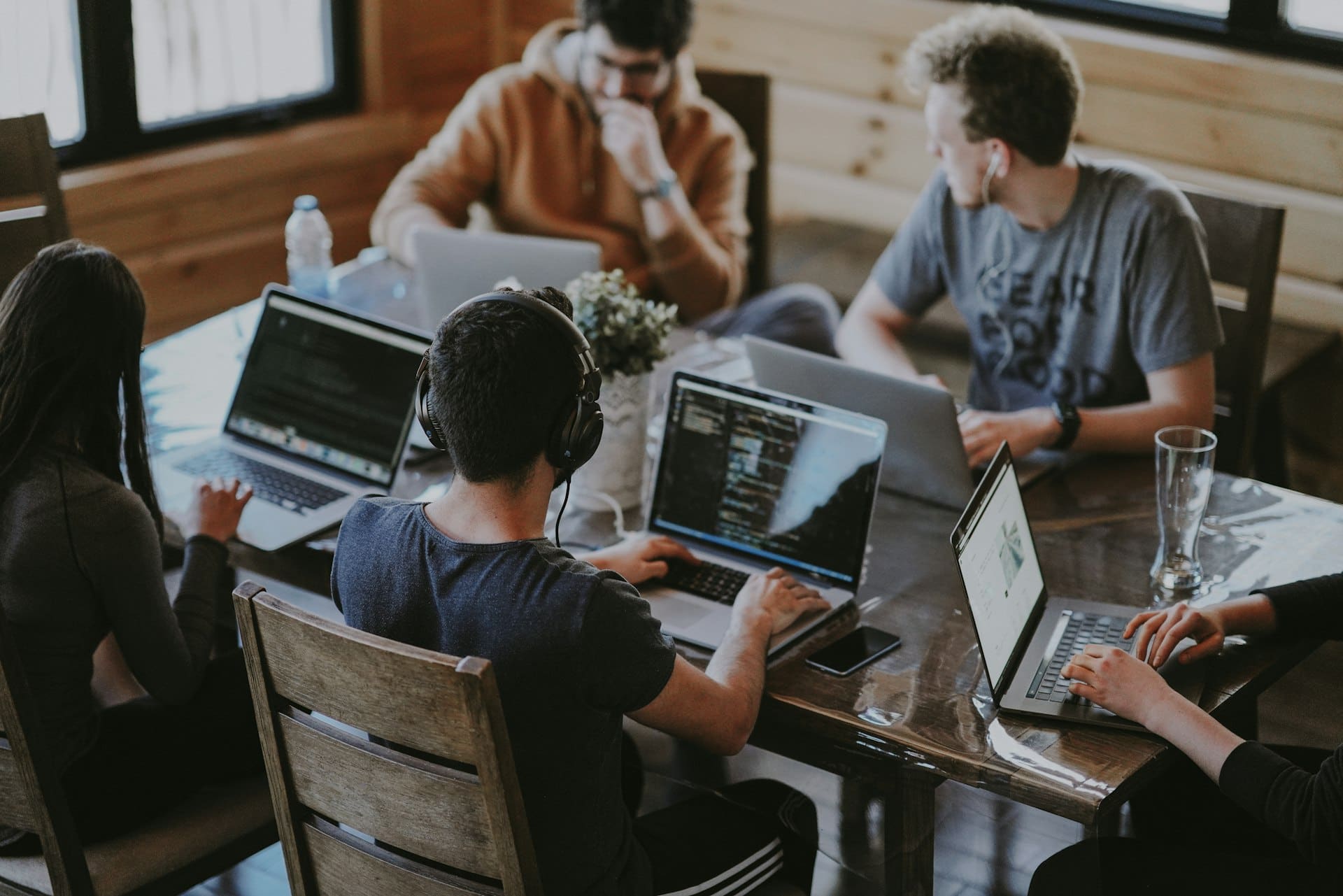 Vier mensen werken samen met laptops aan een houten tafel